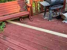 A wooden deck with a bench and a grill on it.