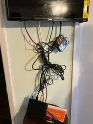 A flat screen tv mounted to a wall with a lot of wires hanging from it.