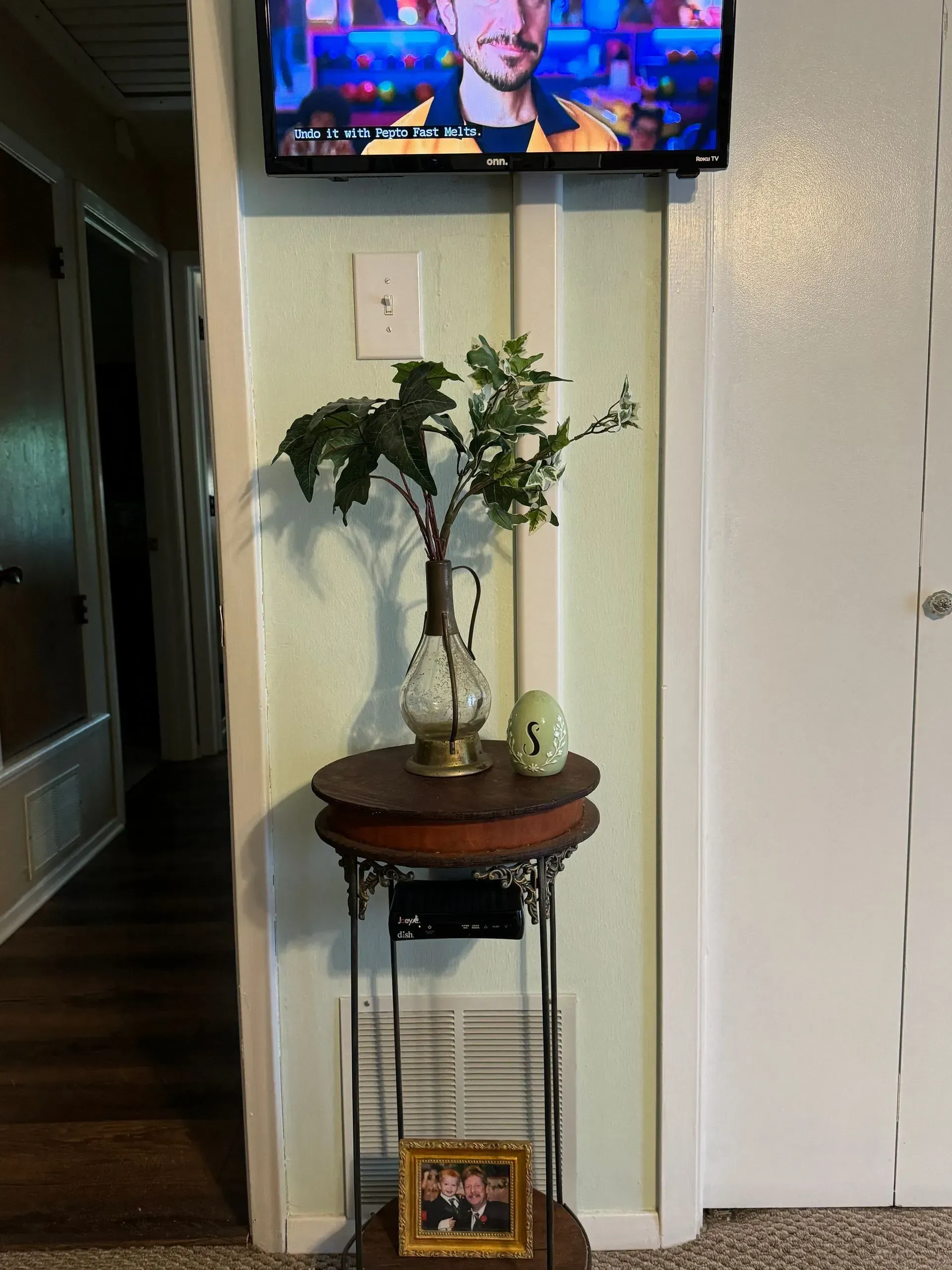 A tv is hanging on a wall next to a table with a vase of flowers on it.