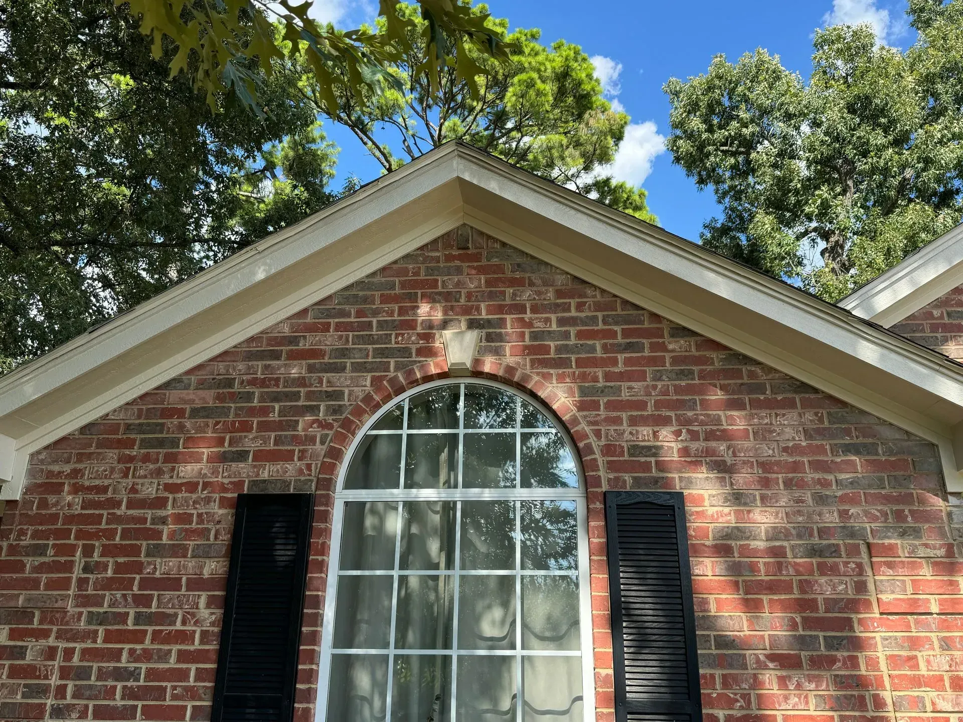 A brick house with a large window and black shutters.