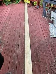 A long piece of wood is sitting on top of a red wooden deck.