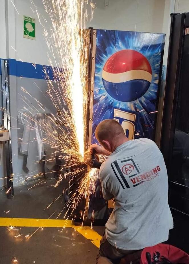 Man cutting a vending machine with sparks flying. Pepsi logo visible.