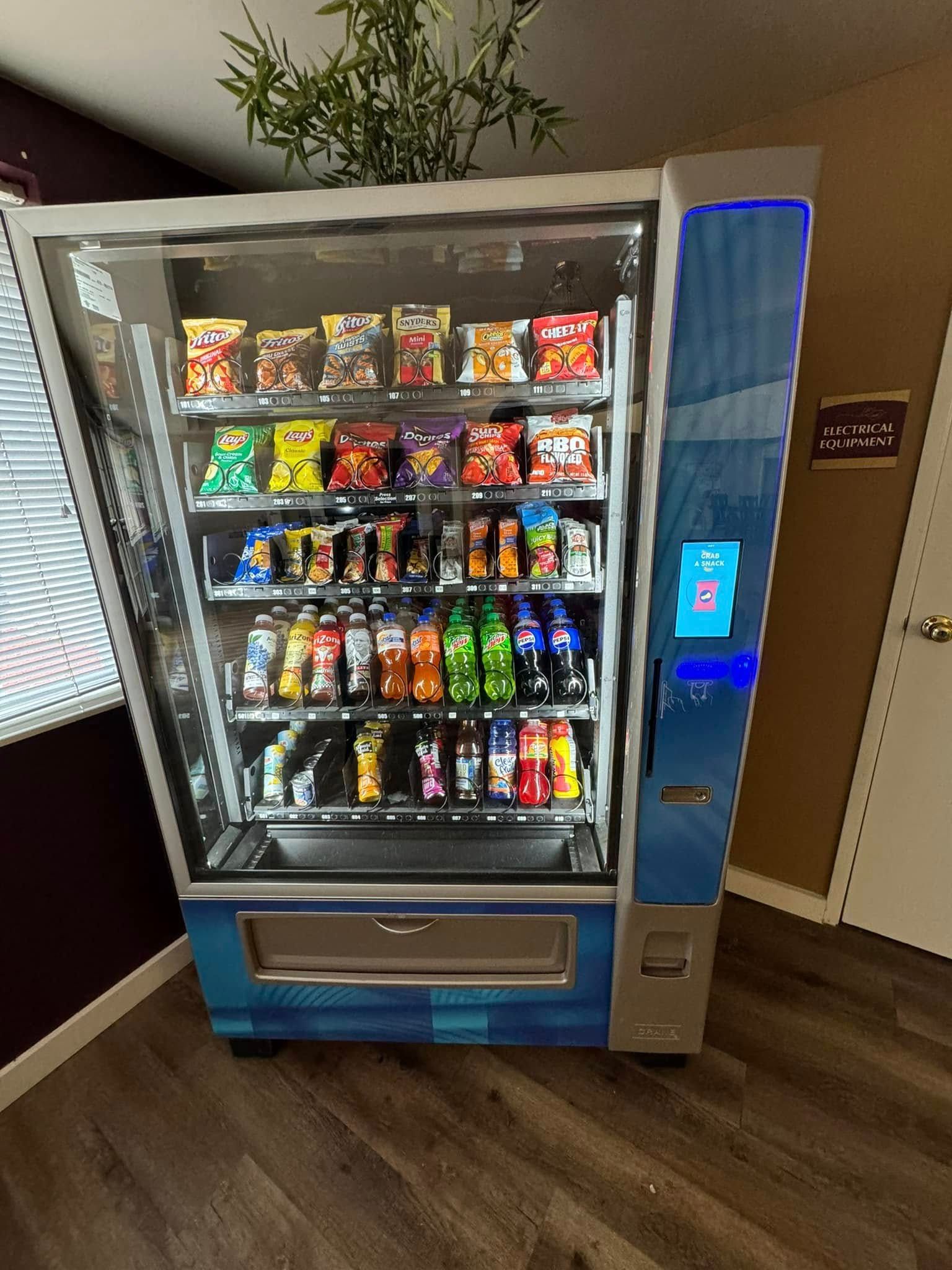 Vending machine with snacks and drinks, blue and silver, in a room.
