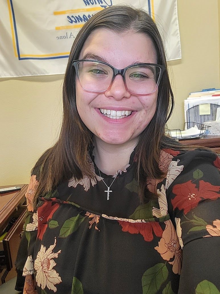 A woman wearing glasses and a cross necklace is smiling for the camera.