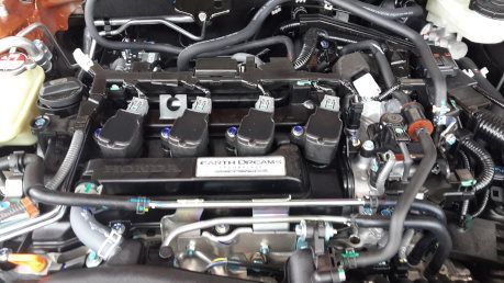 Close-up of a car engine bay with black hoses, wiring, and metal components.