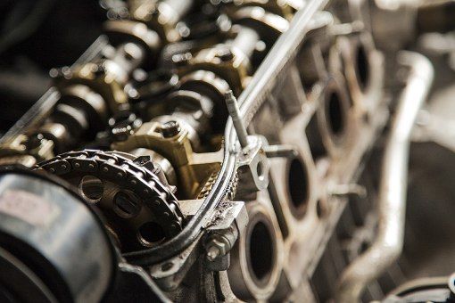 Close-up of a metal engine cylinder head with camshaft, valves, and timing chain exposed