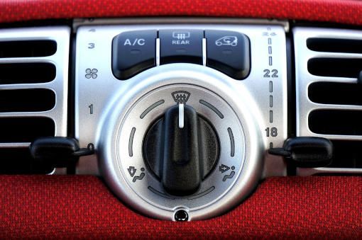Car dashboard climate control knob with silver dial and black buttons on red trim.
