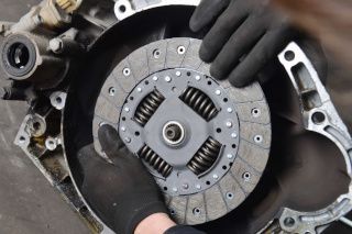 Close-up of a car clutch assembly inside a transmission housing, with a gloved hand holding it.