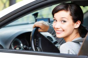 Smiling woman sits in a car, holding the steering wheel and looking back at the camera.