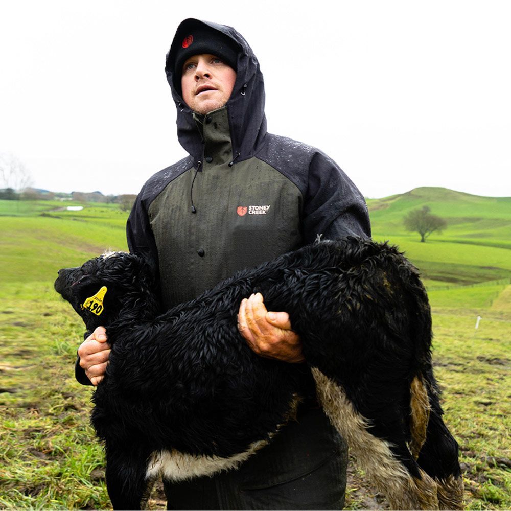 A man in a hooded jacket is holding a black sheep