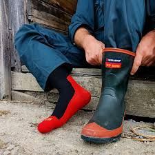 A man is sitting on the ground tying his rain boots.