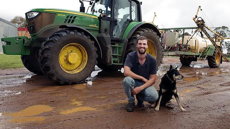 A man is kneeling next to a dog in front of a john deere tractor.