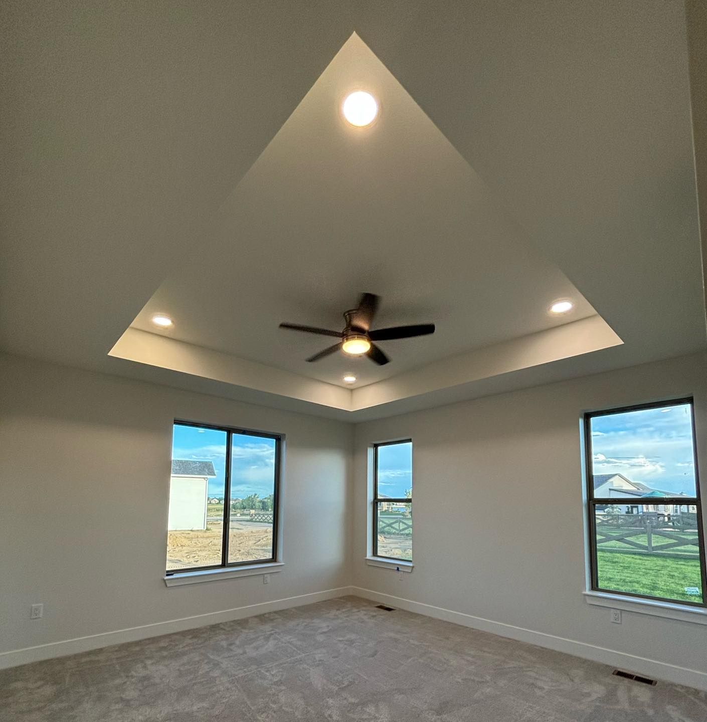 Bedroom interior with tray ceiling, recessed lighting, and ceiling fan. Windows offer an outside view.