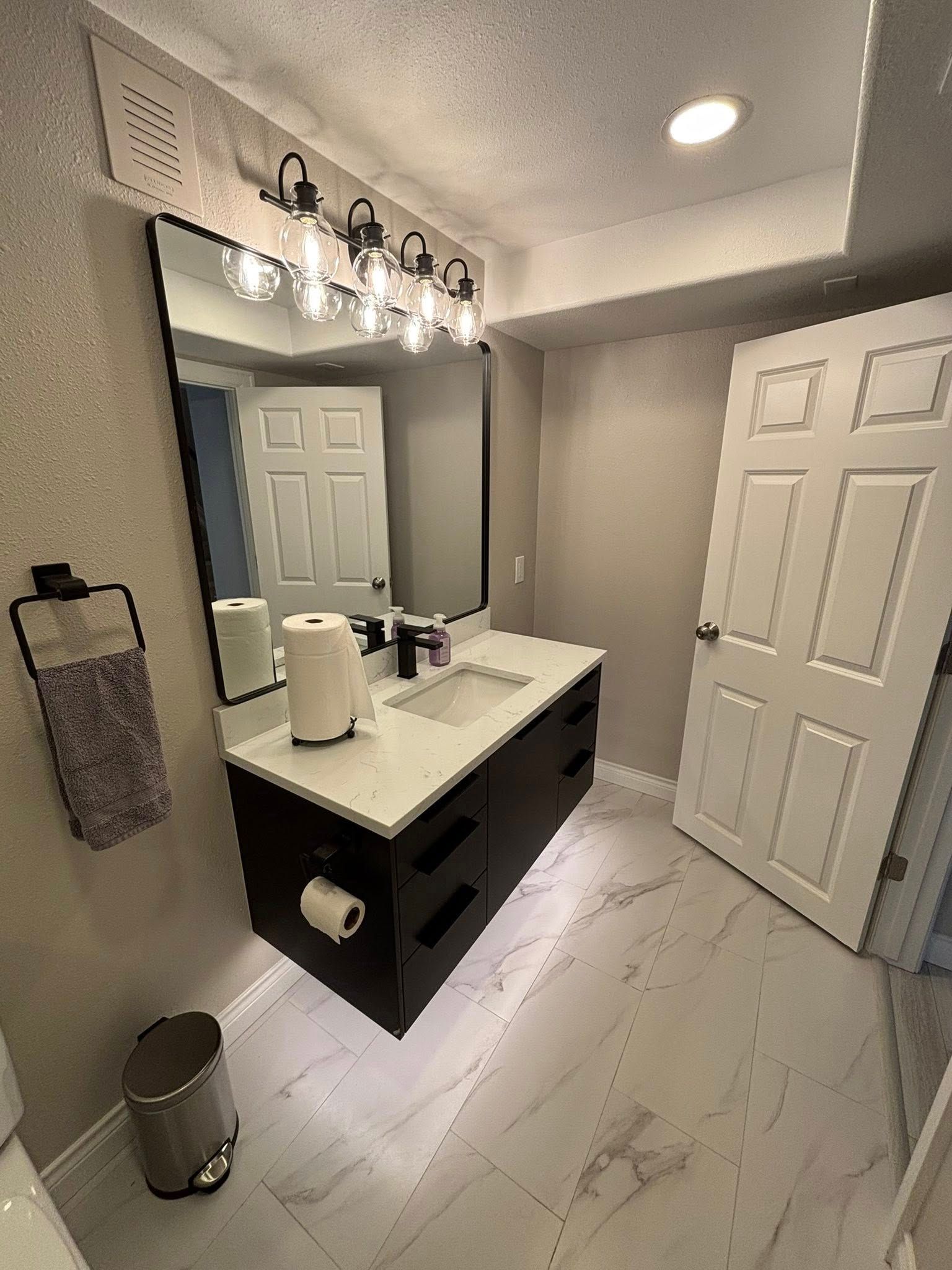 Modern bathroom with dark floating vanity, large mirror, and white tile floor.