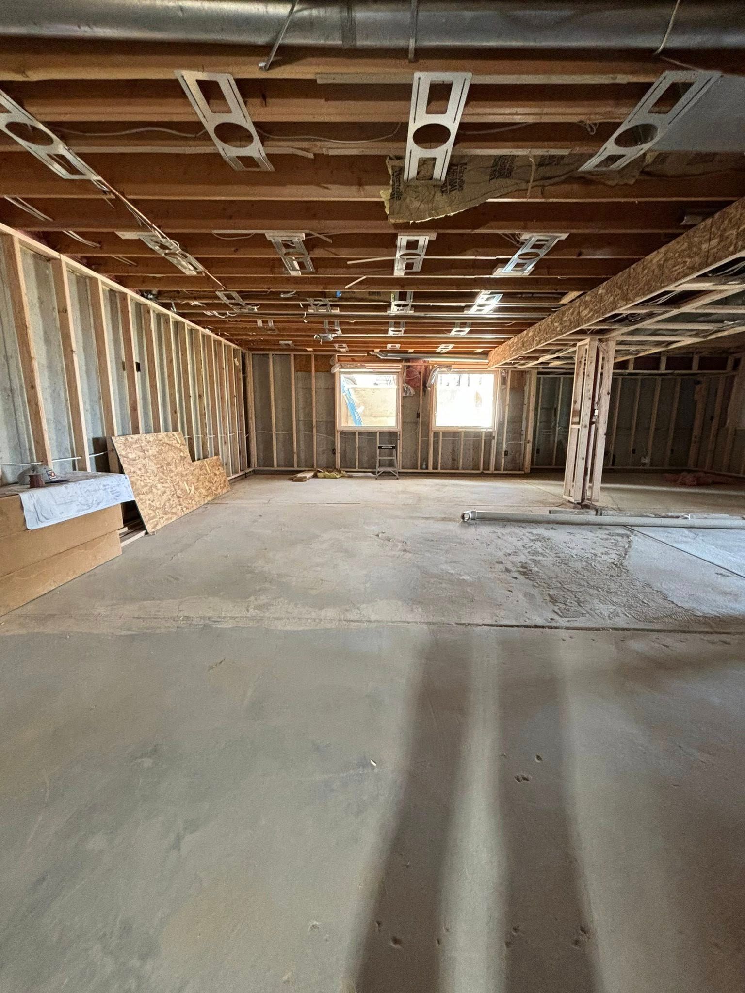 Unfinished basement with concrete floor, exposed framing, and two windows.