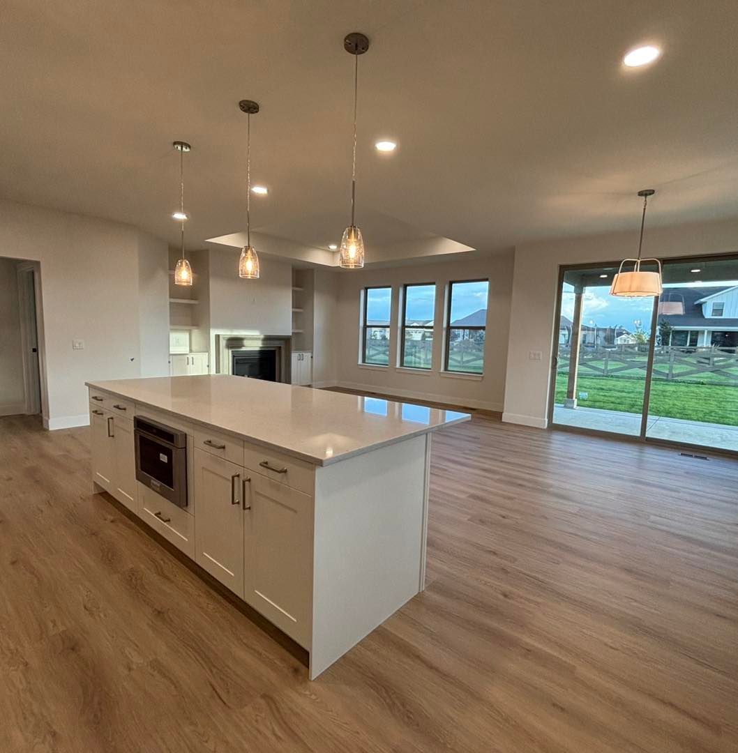 Modern kitchen with white island, pendant lights, and open to living space with large windows.