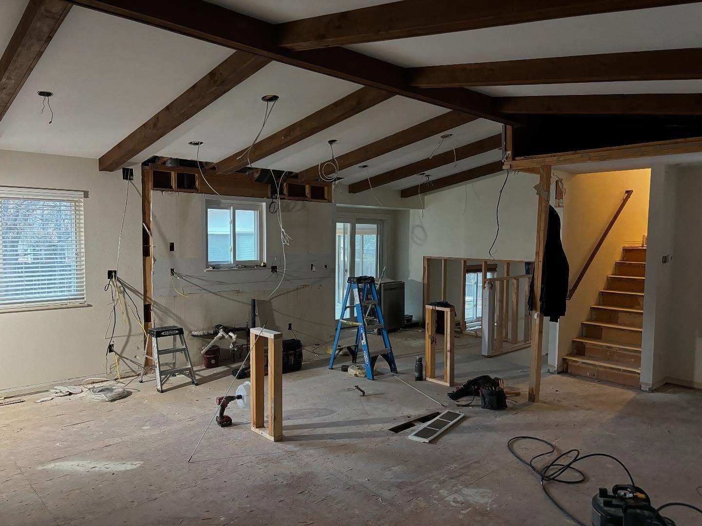 Interior undergoing renovation: exposed beams, wires, framing, and stairs.