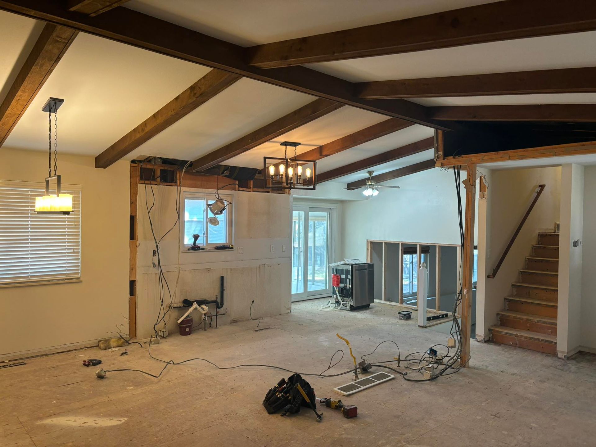 Interior renovation: open-concept living space, exposed walls, ceiling beams, wiring, and a staircase.