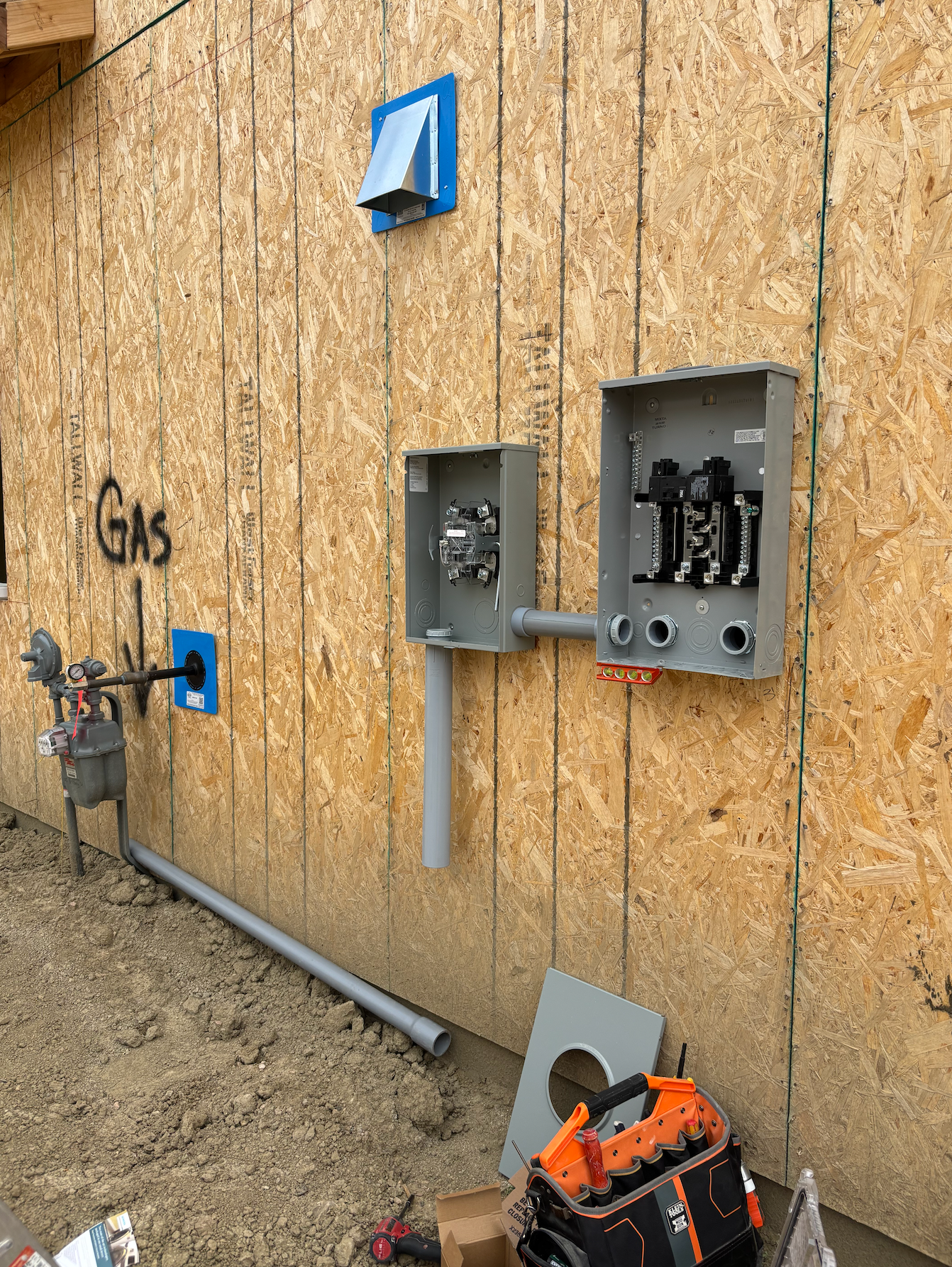 Exterior wall with electrical and gas utilities installed; gray conduit, boxes, vent.