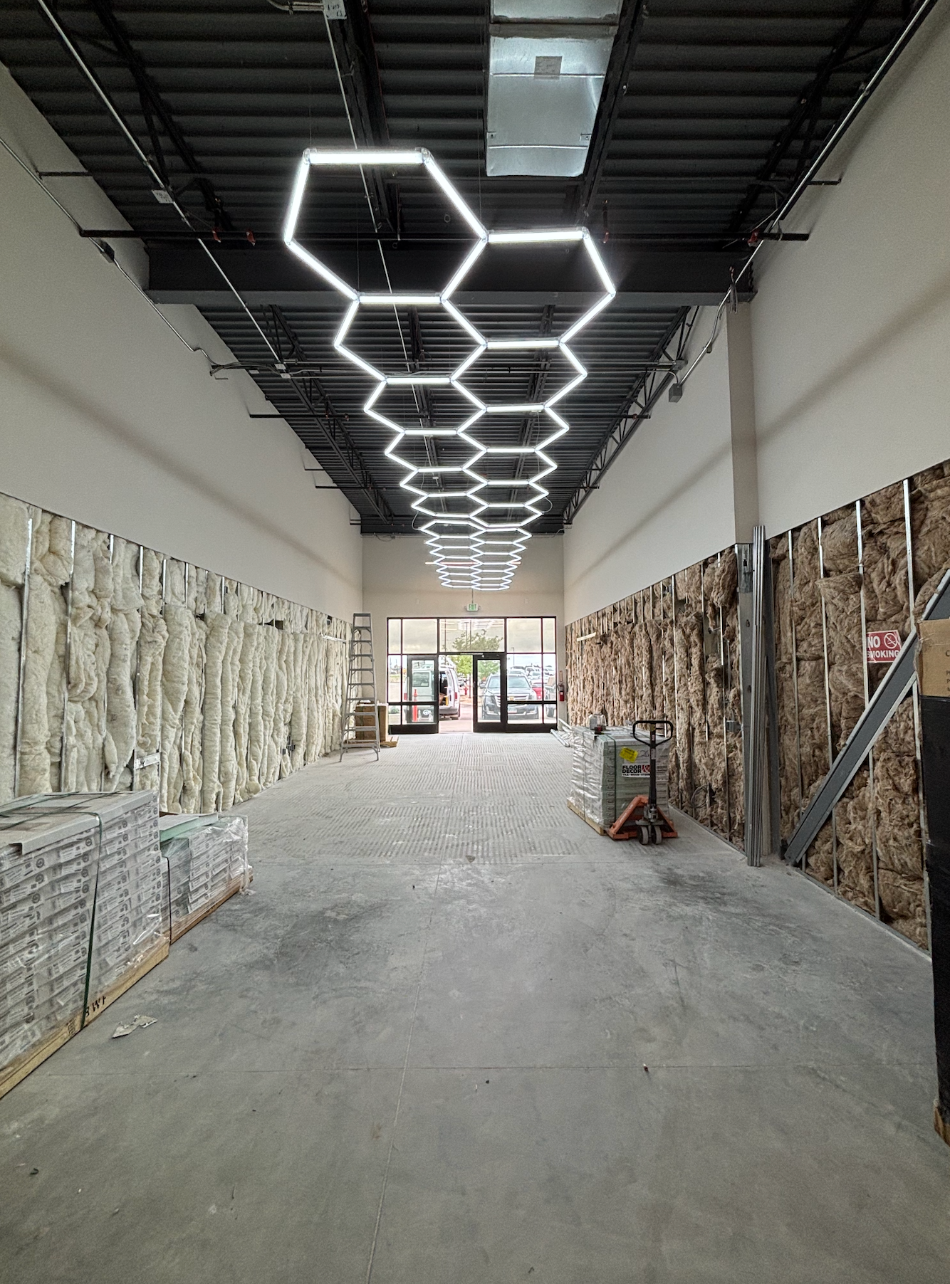Open-plan living area with white cabinets, island, wood beams, seating, dining table, stairs, and a light gray rug.