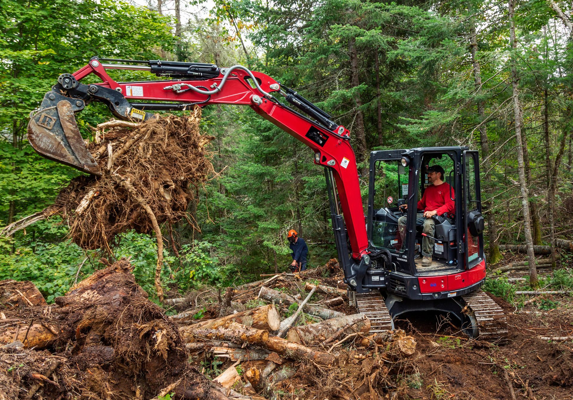 Un homme conduit une excavatrice rouge dans les bois.