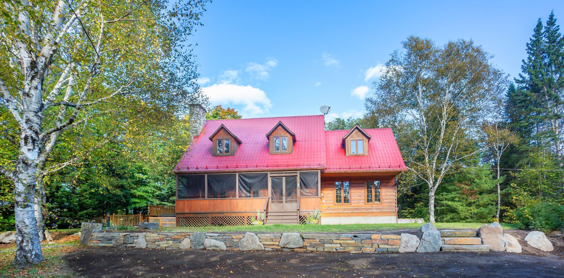 Une grande cabane en rondins avec un toit rouge est entourée d'arbres.
