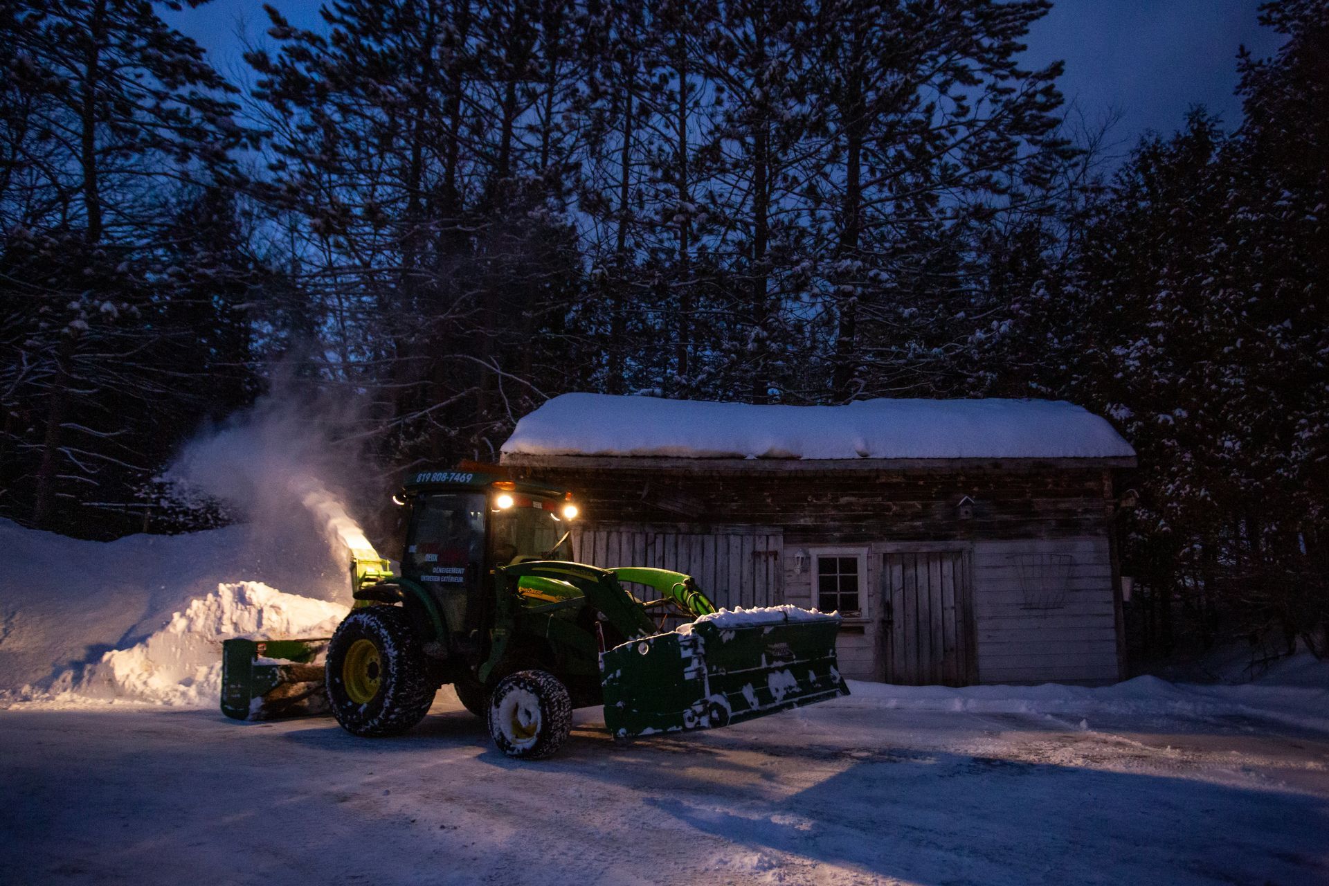 Un tracteur souffle la neige devant un bâtiment la nuit.