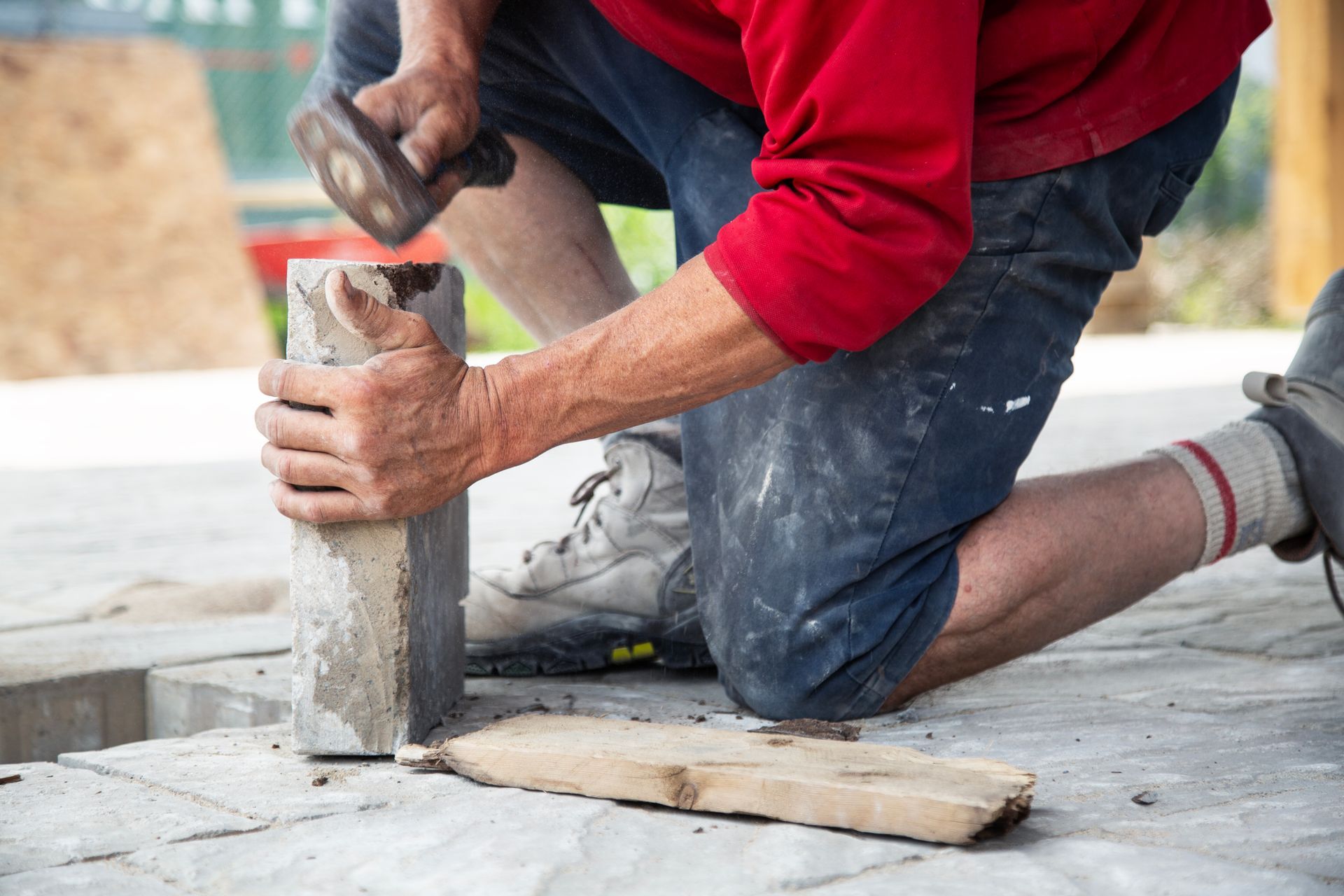 Un homme est à genoux et tient une brique avec un marteau.