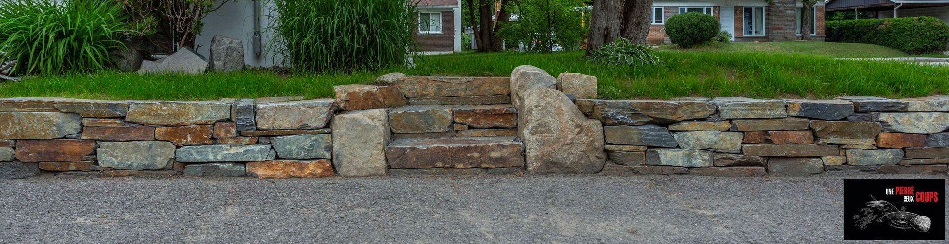 Un mur de pierre se trouve sur le côté de la route devant une maison.