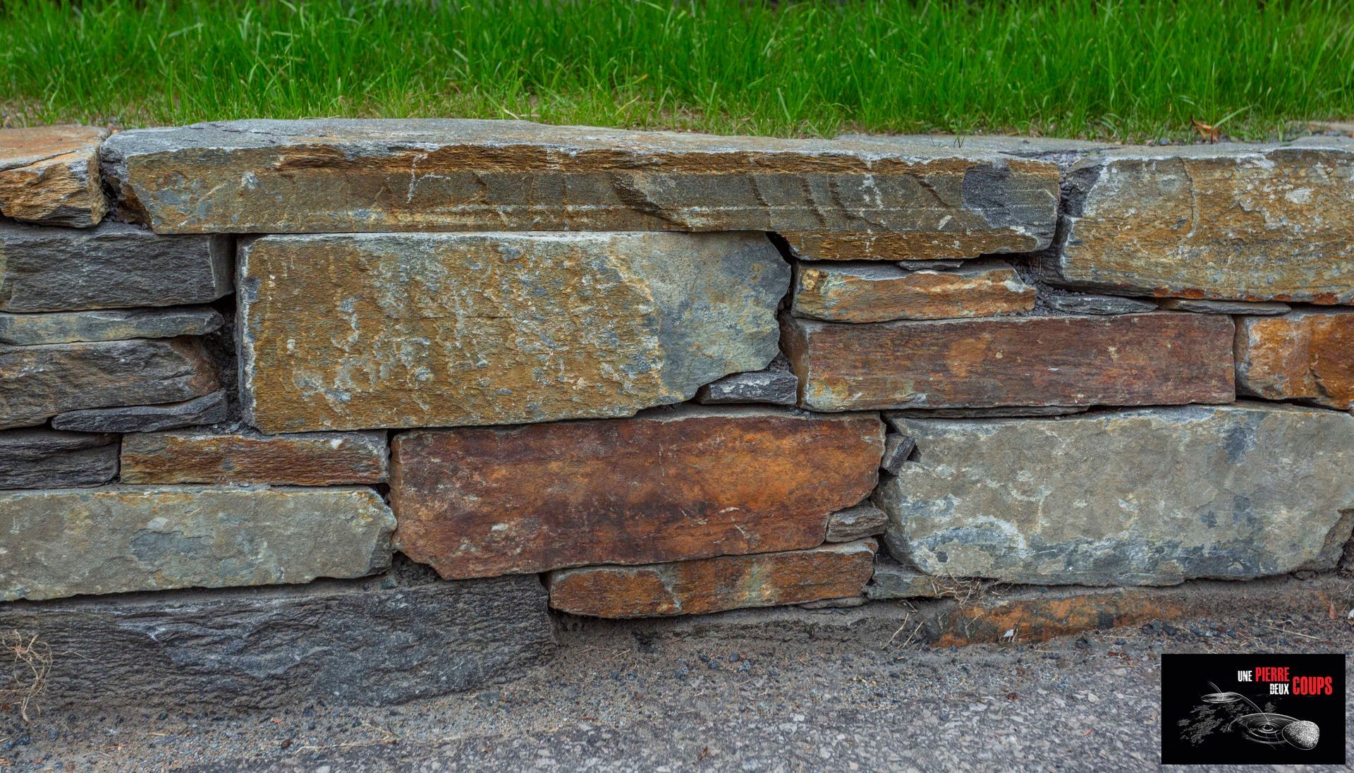 Un gros plan d'un mur de pierre avec de l'herbe en arrière-plan.