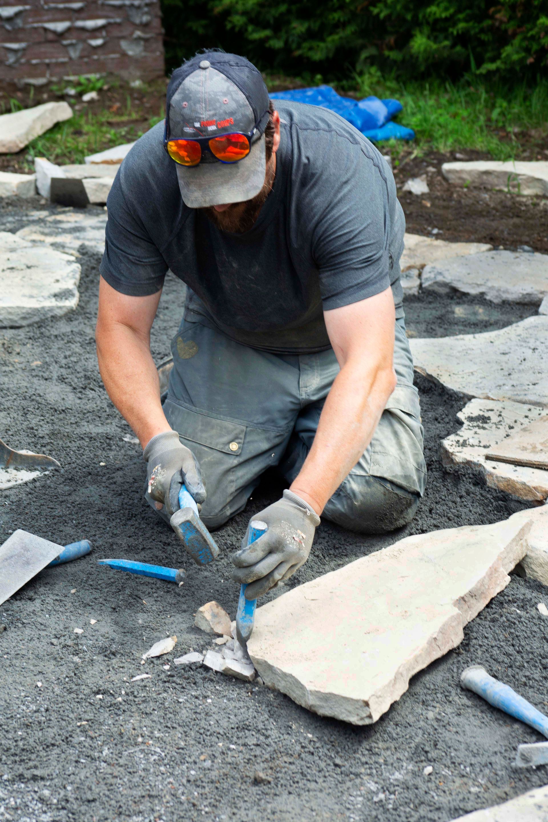 Un homme est à genoux alors qu'il travaille sur une passerelle en pierre.