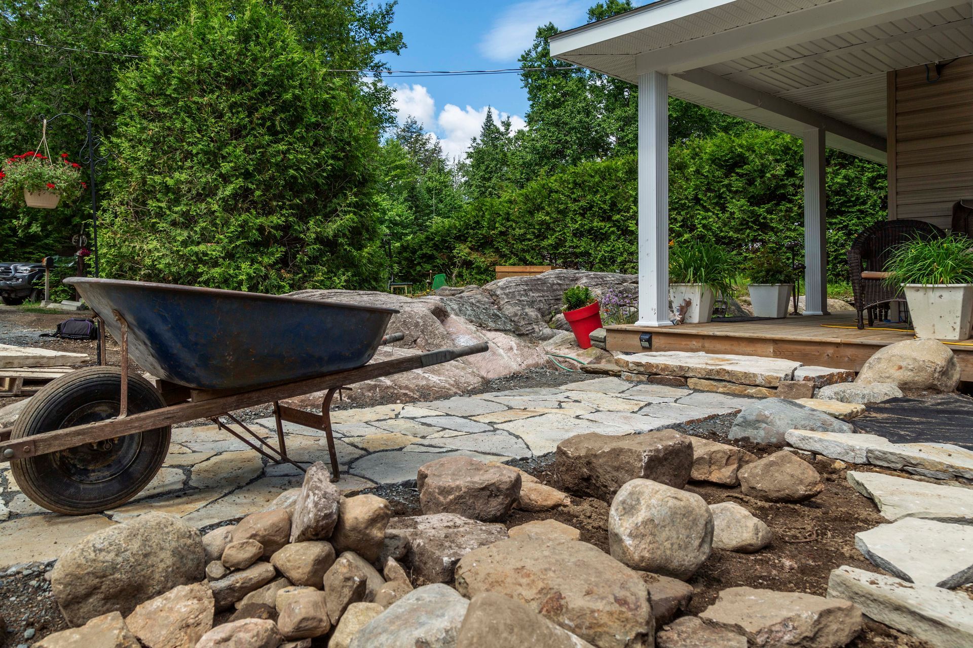 Une brouette est posée sur un tas de rochers devant une maison.