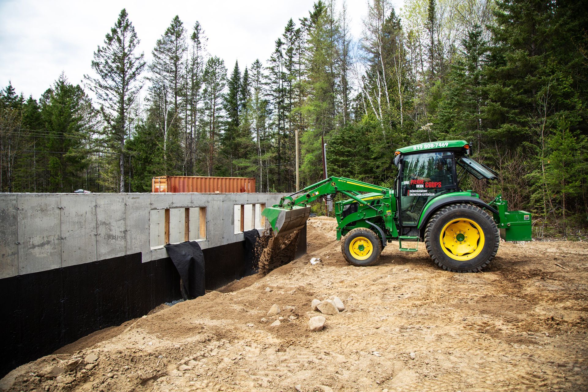 Un tracteur vert et jaune roule sur un chemin de terre.