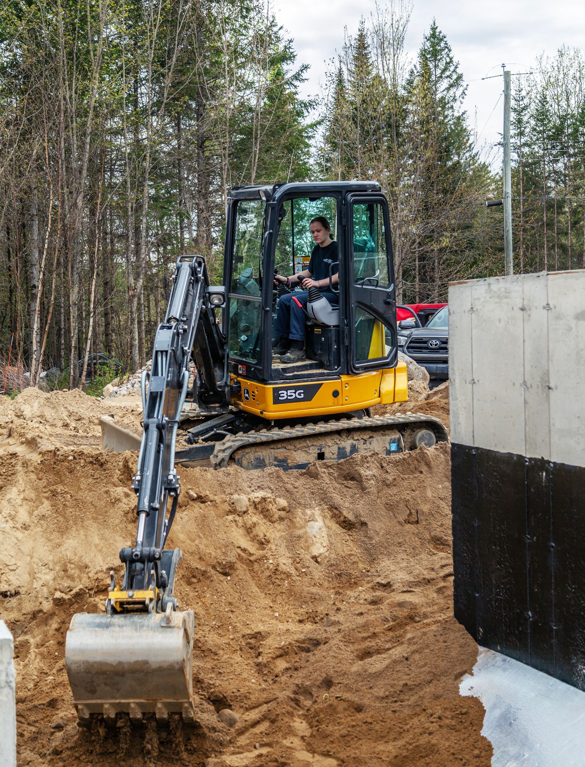 Un homme conduit une petite excavatrice sur un chemin de terre.