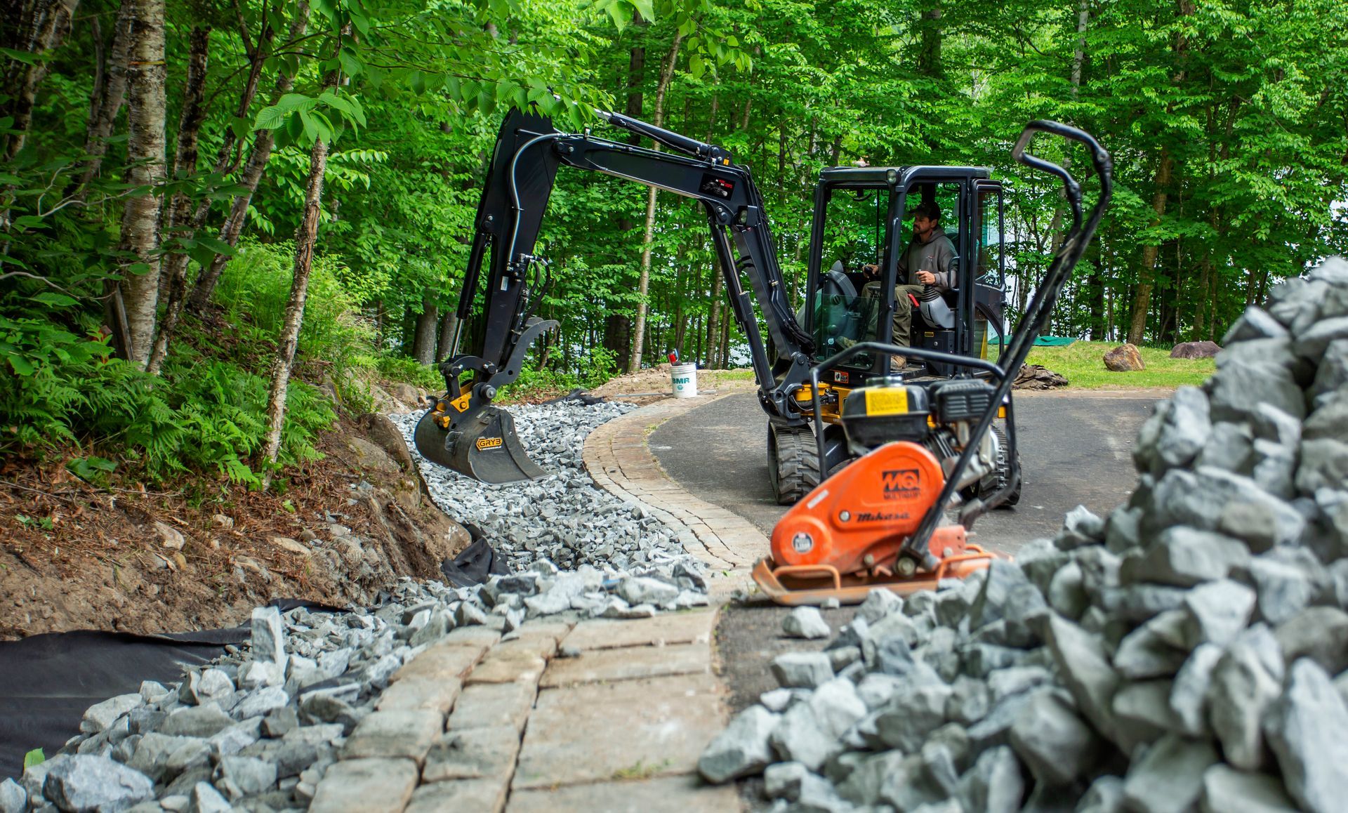 Un homme conduit une excavatrice sur un chemin de terre à côté d'un tas de rochers.