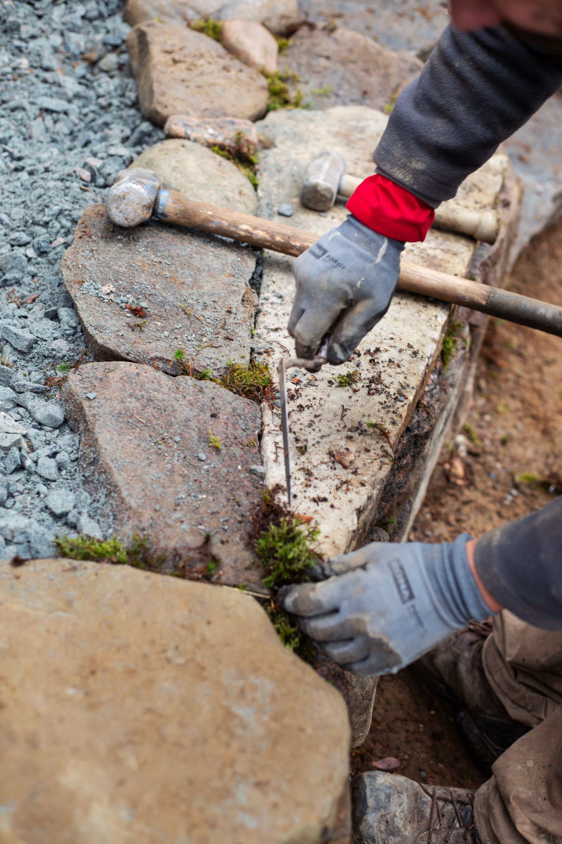 Une personne travaille sur un trottoir en pierre avec un marteau et une pelle.