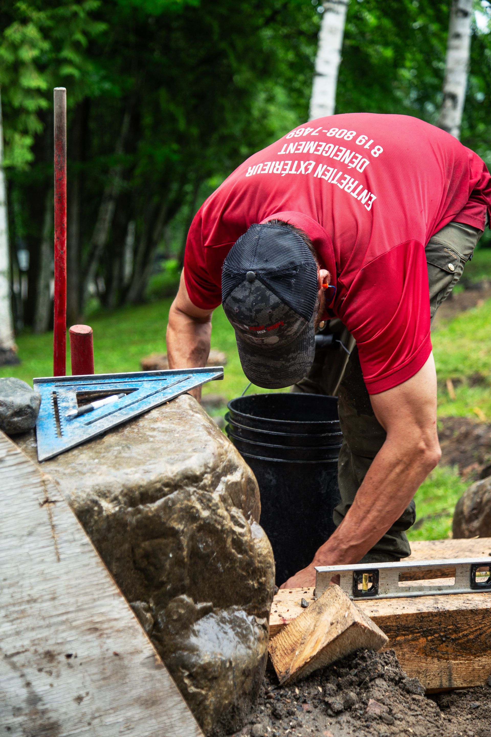 Un homme en chemise rouge travaille sur un mur de pierre.