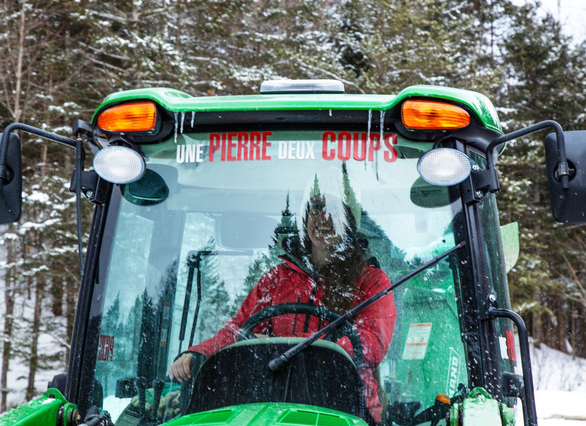 Un homme conduit un tracteur vert dans la neige.