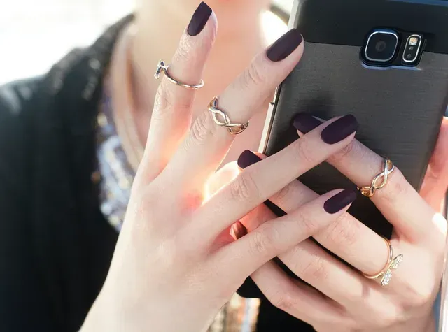 Een vrouw met paarse nagels houdt een mobiele telefoon vast
