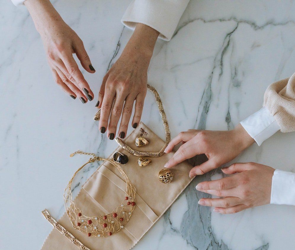 Twee vrouwen stoppen sieraden in een tas op een tafel.