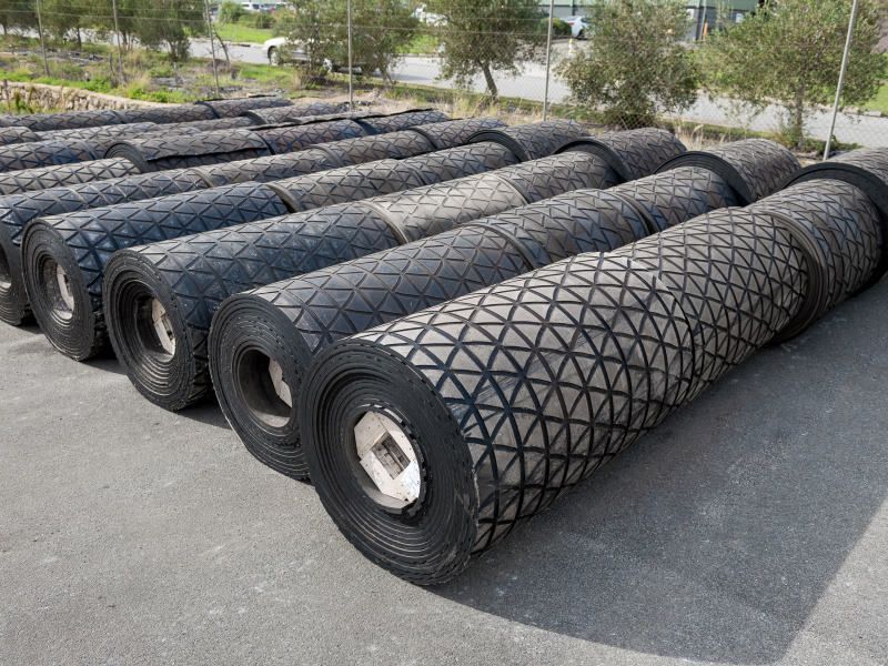 Rouleaux de matériau de bande transporteuse noire avec divers motifs texturés, empilés à l'extérieur.