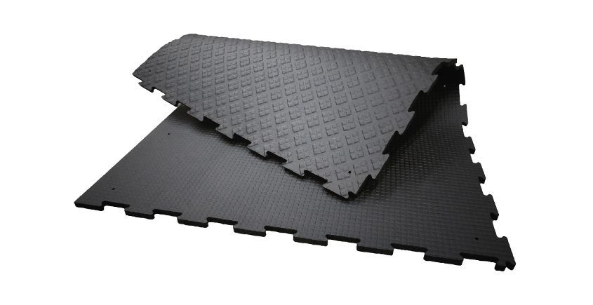 Tapis de sol en caoutchouc noir emboîtables à surface texturée. Un tapis est partiellement soulevé, révélant les bords emboîtables.