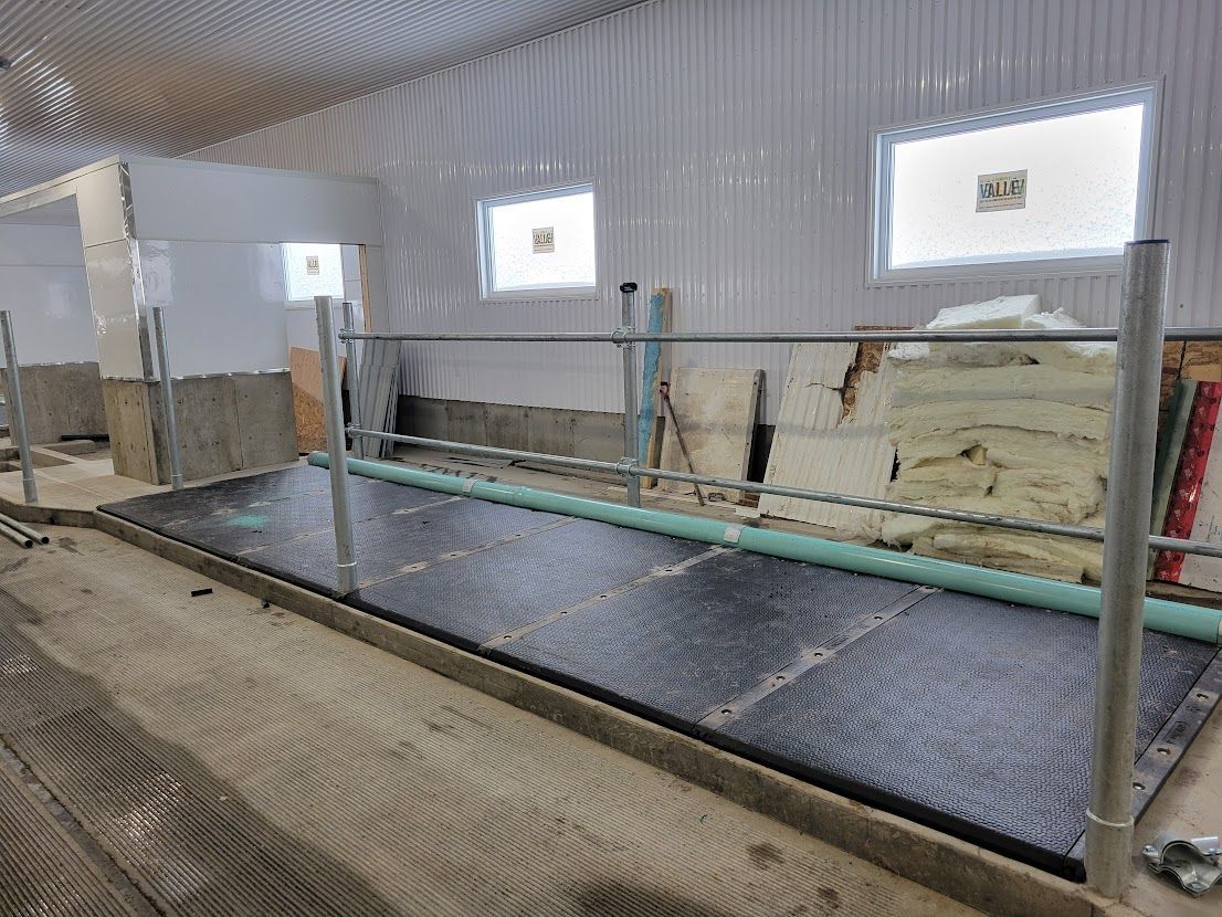 Intérieur d'une grange en construction, montrant une rangée d'étals avec une ossature métallique et un revêtement de sol sombre.