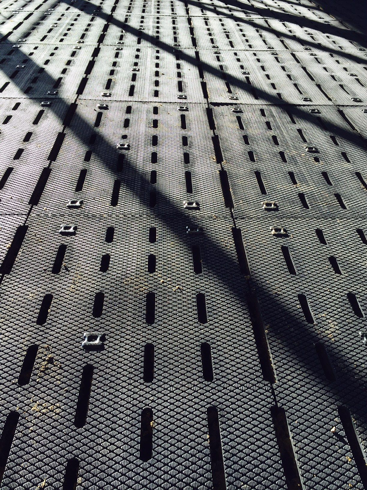 Une grille métallique dotée de fentes longues et étroites projette une ombre sombre et géométrique sur sa surface à la lumière du soleil.