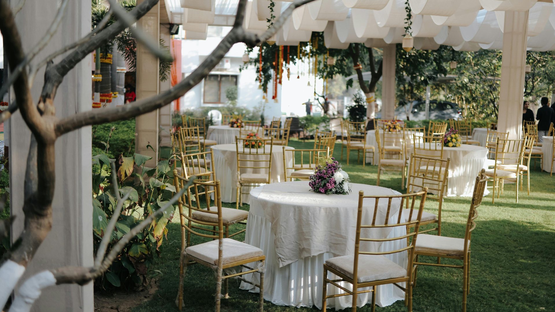A row of white folding chairs and tables on a lush green field.