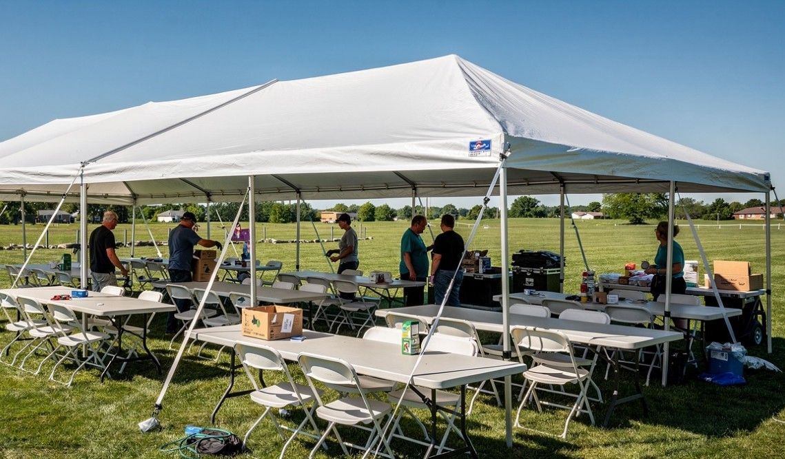 A white tent with tables and chairs underneath it in a field.