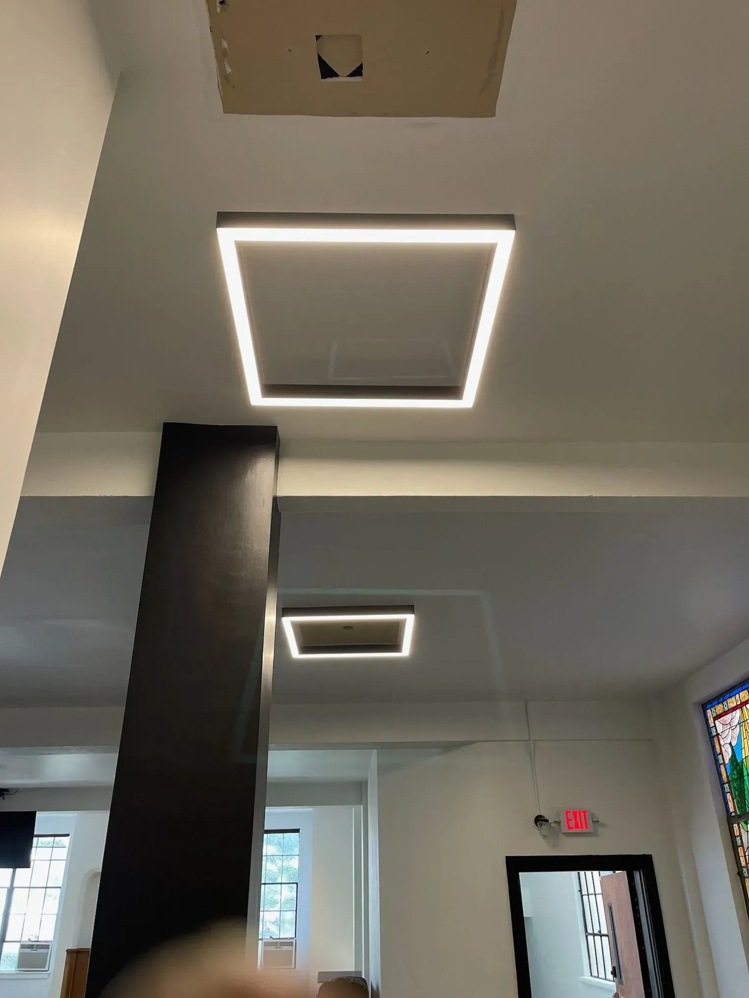 Square LED ceiling lights illuminate an interior space with a black pillar and doorway.