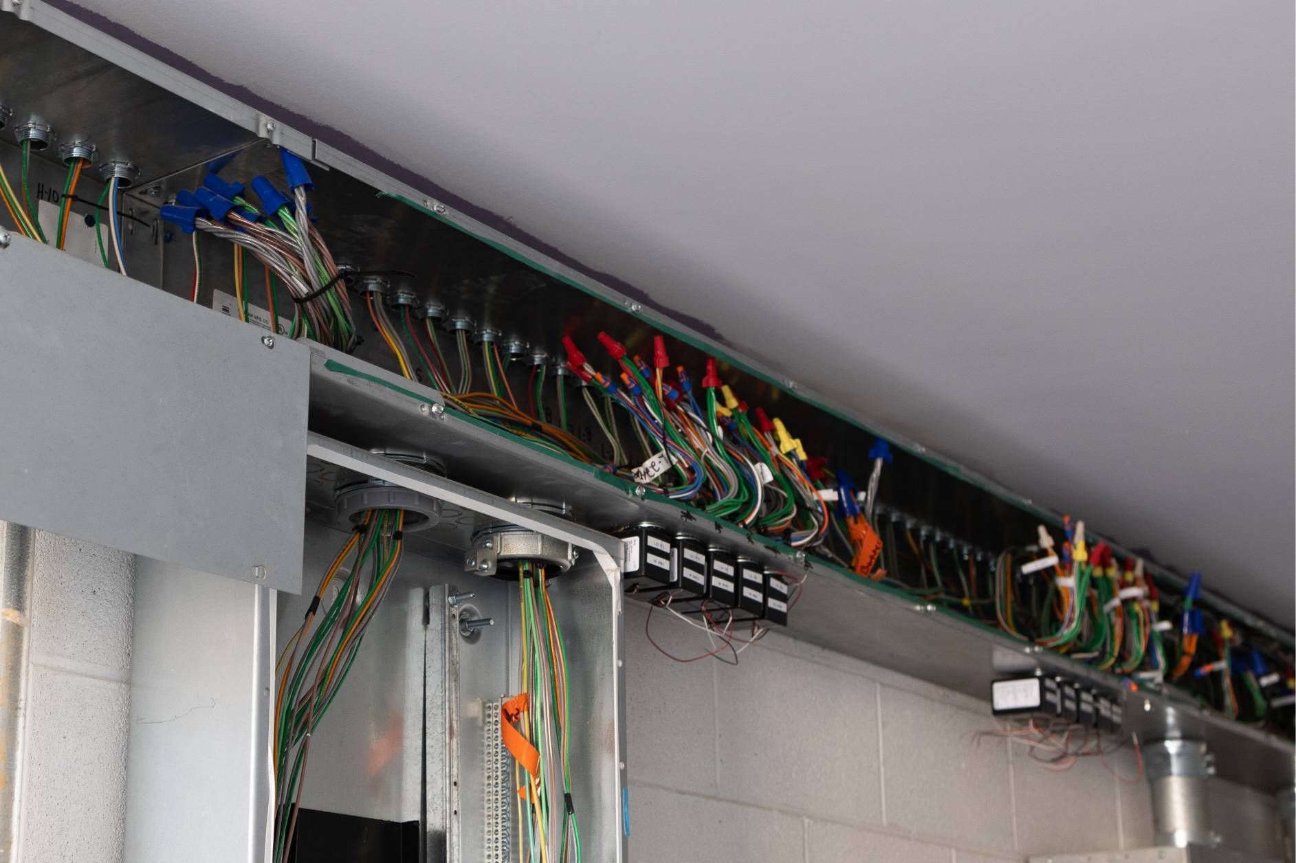 Electrical wiring in metal conduit and junction boxes along a wall.