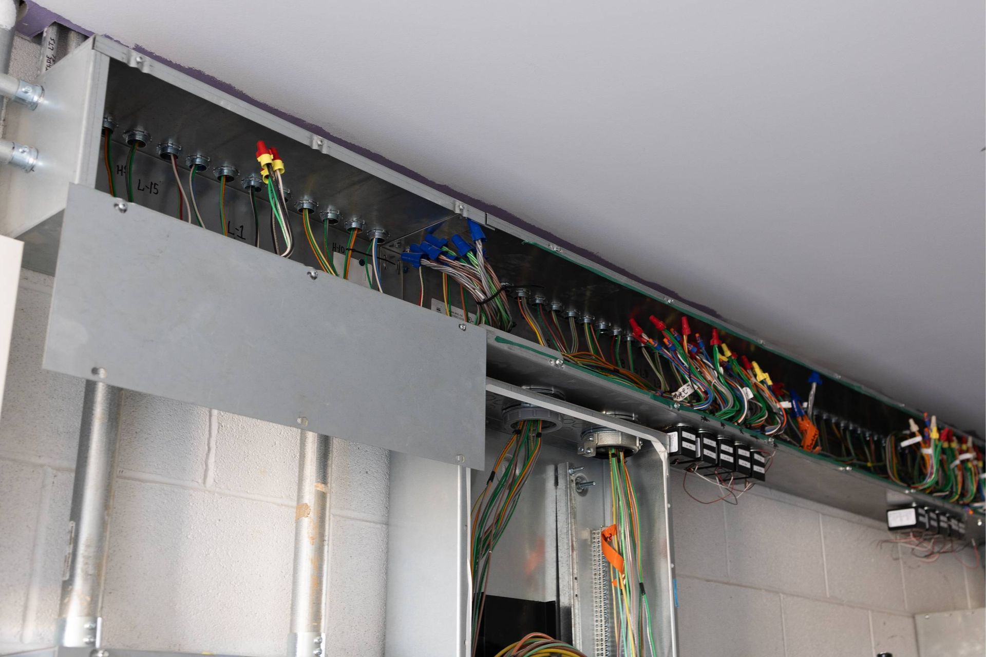 Electrical wiring in a gray metal enclosure, mounted along a wall. Wires are various colors.