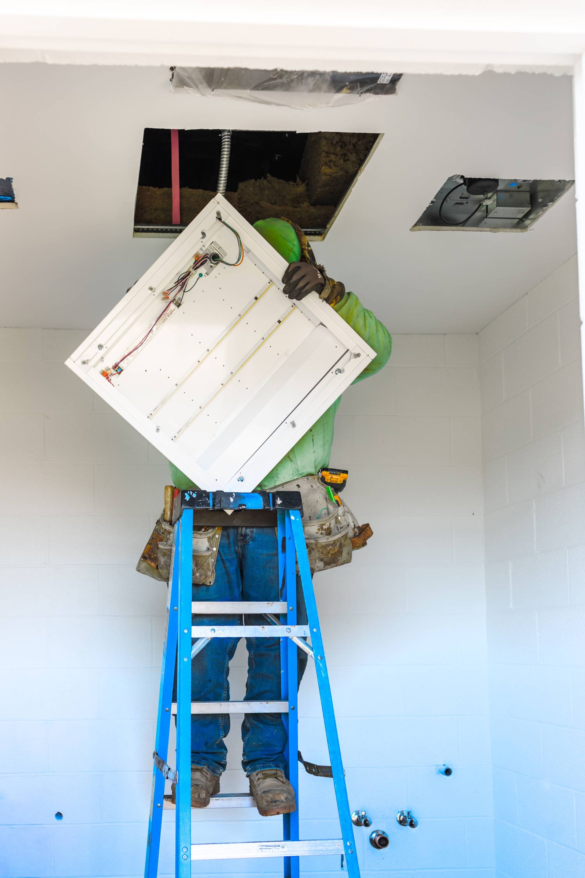 Person on a ladder removing a ceiling panel in a room.